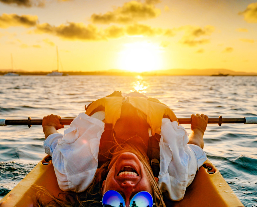 Smiling woman laying back on a kayak at sunset